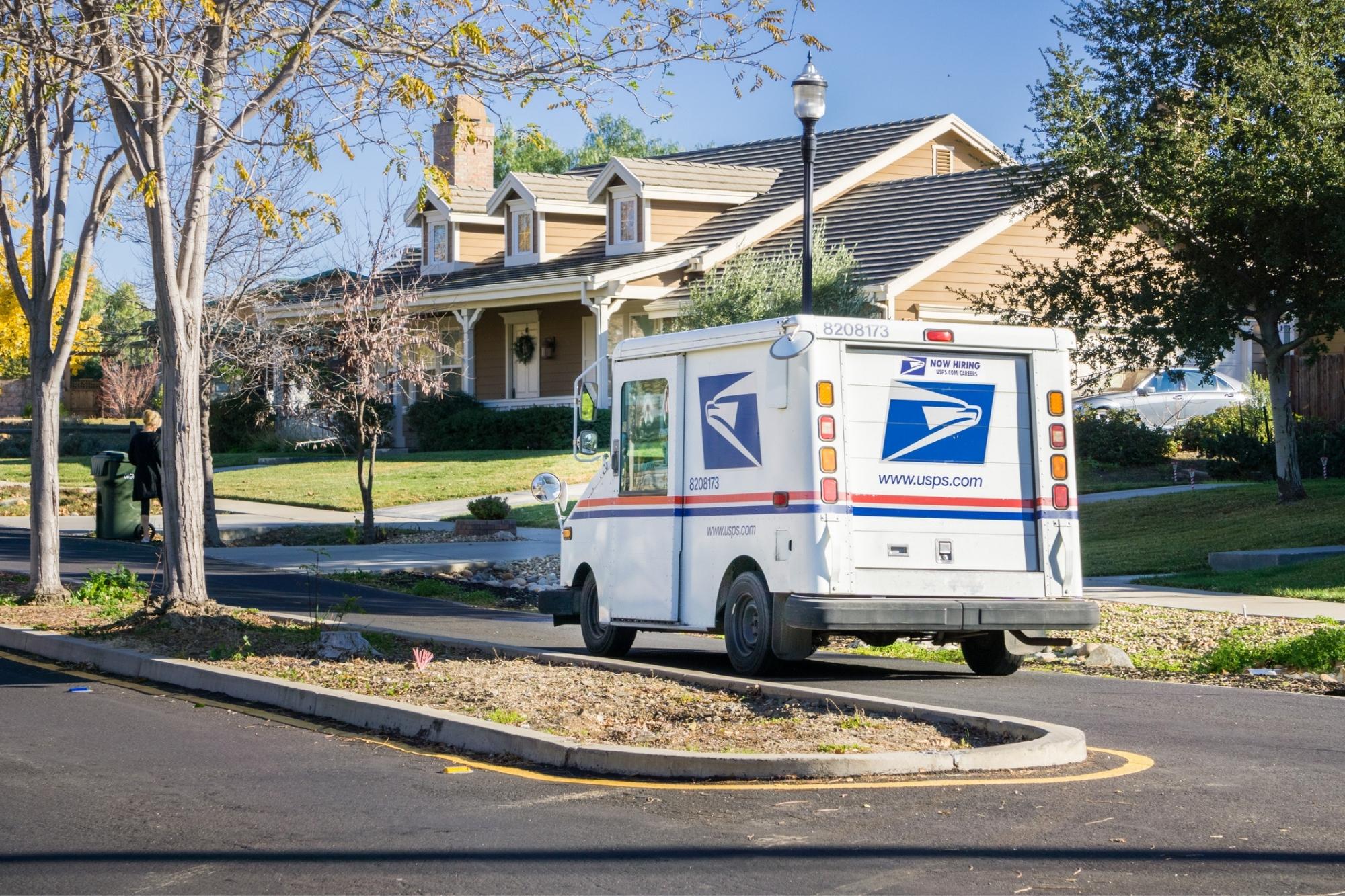 A USPS truck delivering mail in a neighborhood.